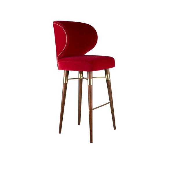 A high-resolution photograph of the Louis bar chair by Ottiu, showcasing its profile view. The chair features an upholstered body in a luxurious deep red velvet, bordered by a thin metallic piping that follows the curve of the crescent-shaped backrest. Its tall, tapered legs and support frame are crafted from rich, dark smoked walnut wood. Polished brass connectors and footrests bridge the wooden legs, adding a modern and elegant accent. The chair is positioned to clearly display the side profile of the seat, back, and the complex leg structure.
