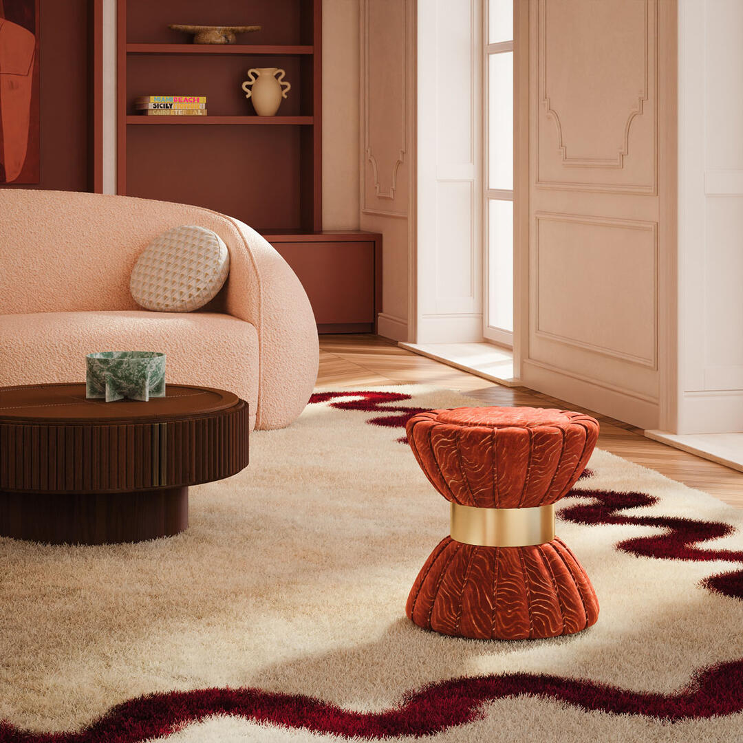 Colette Stool by Ottiu, upholstered in vibrant orange patterned Casamance fabric with a brushed brass base, showcasing a bold yet elegant design. Placed in a soft-toned living room beside the Robert center table and the Peggy sofa.