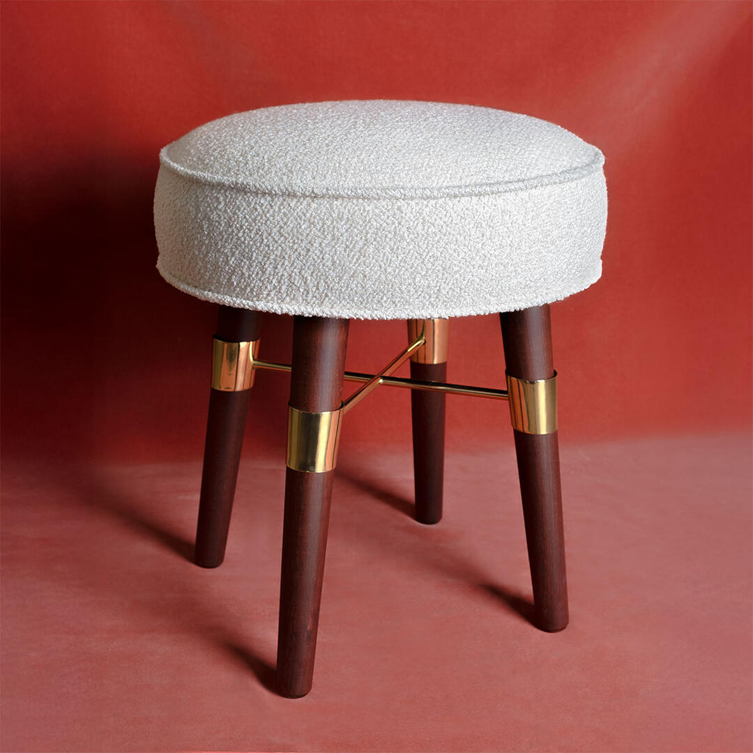 Louis Stool upholstered in white bouclé fabric, featuring smoked walnut wood legs with polished brass details, set against a salmon background.