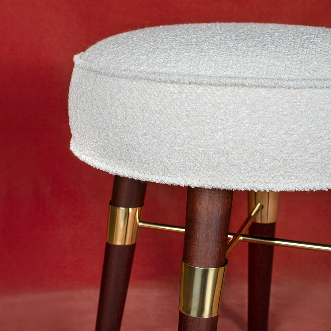 Close-up of the Louis Stool showcasing the white bouclé upholstery, smoked walnut wood, and polished brass details, highlighting the textures and material craftsmanship.