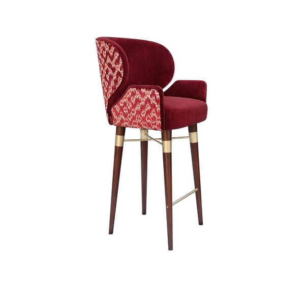 A side view of the Ottiu Louis I bar chair, showing the solid red velvet interior and seat. The side and back feature the patterned Schumacher Antique Strie Velvet in redwood. The dark wood legs have brushed brass details and a footrest.