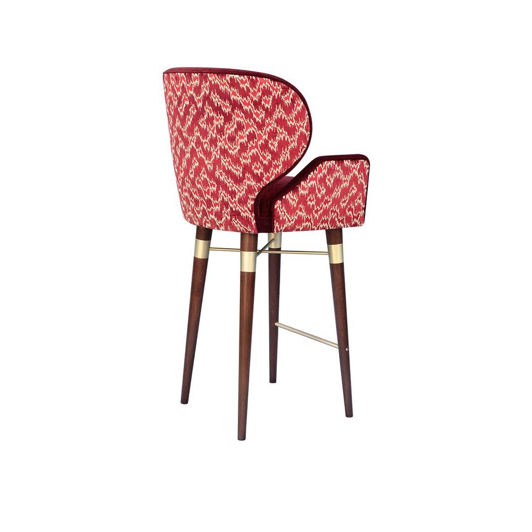 A back three-quarter view of the Ottiu Louis I bar chair, highlighting the patterned Schumacher Antique Strie Velvet in redwood. The dark wood legs are prominent, with brushed brass details at the top.