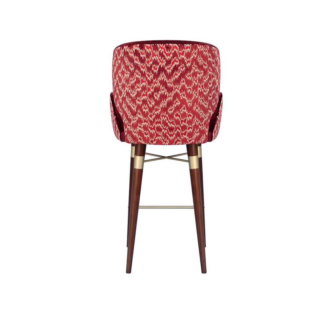 A back view of the Ottiu Louis I bar chair, showcasing the patterned Schumacher Antique Strie Velvet in redwood. The dark wood legs feature brushed brass accents at the top.