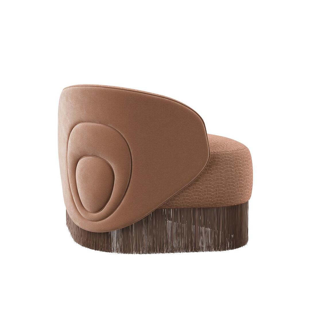 Doris armchair shown from a 45º back angle. The piece highlights a lavish composition, exquisitely hand-upholstered in sumptuous orange velvet fabrics, elegantly draped with cascading fringes that exude grandeur. Upholstered in Dedar fabrics: Ripley and Plushy.
