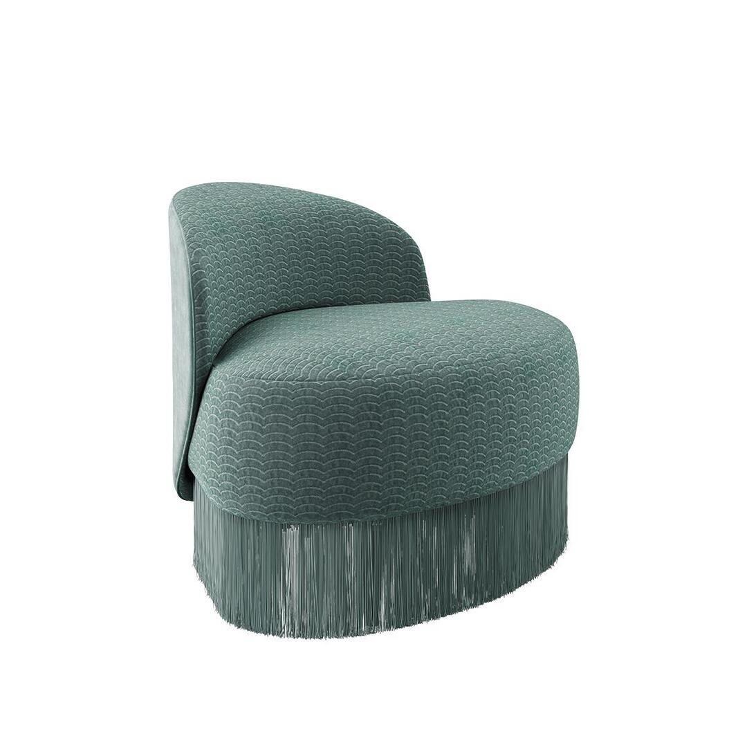 Doris armchair shown from a 45º front angle. The piece highlights a lavish composition, exquisitely hand-upholstered in sumptuous turquoise velvet fabrics, elegantly draped with cascading fringes that exude grandeur. Upholstered in Dedar fabrics: Ripley and Plushy.