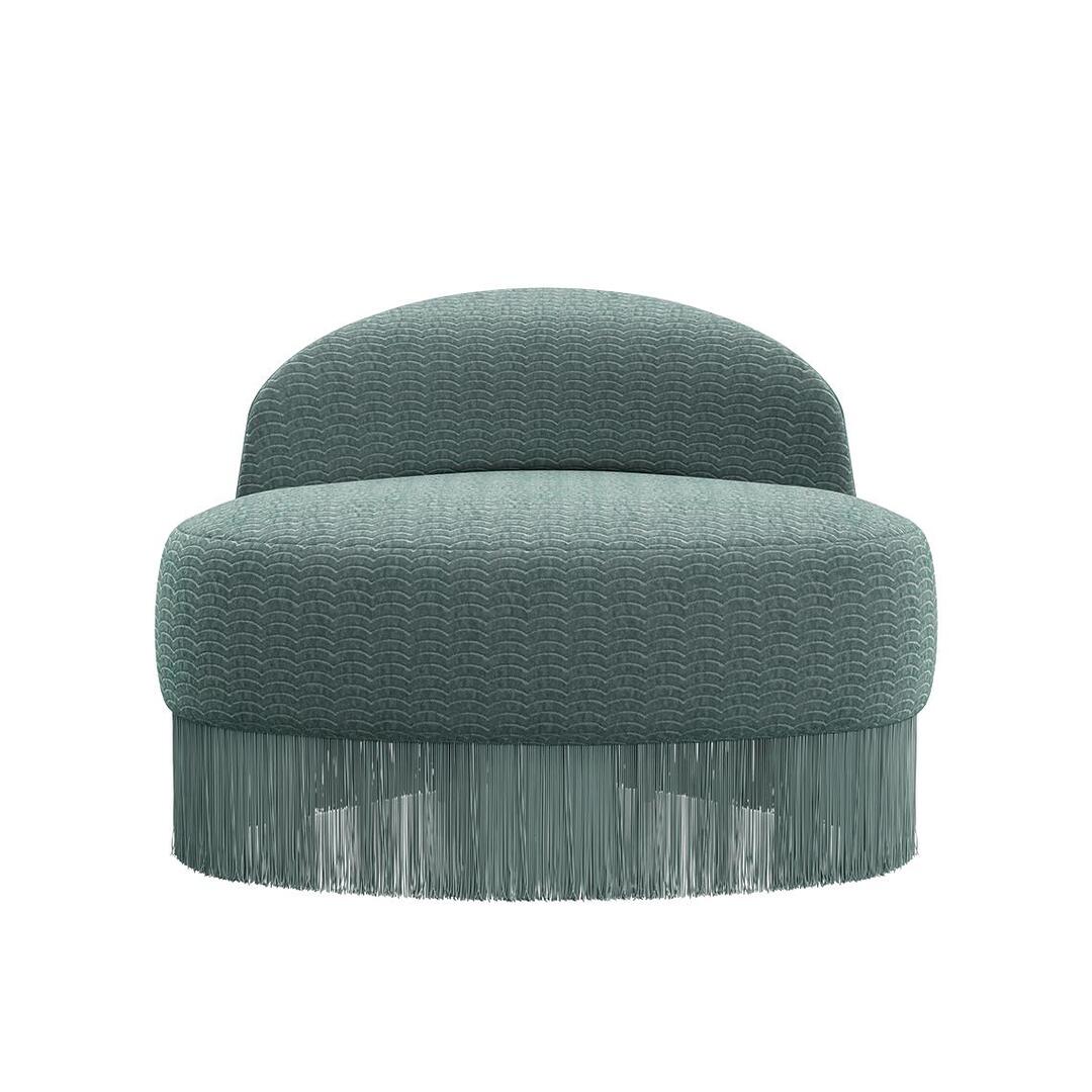 Doris armchair shown from a front view. The piece highlights a lavish composition, exquisitely hand-upholstered in sumptuous turquoise velvet fabrics, elegantly draped with cascading fringes that exude grandeur. Upholstered in Dedar fabrics: Ripley and Plushy.
