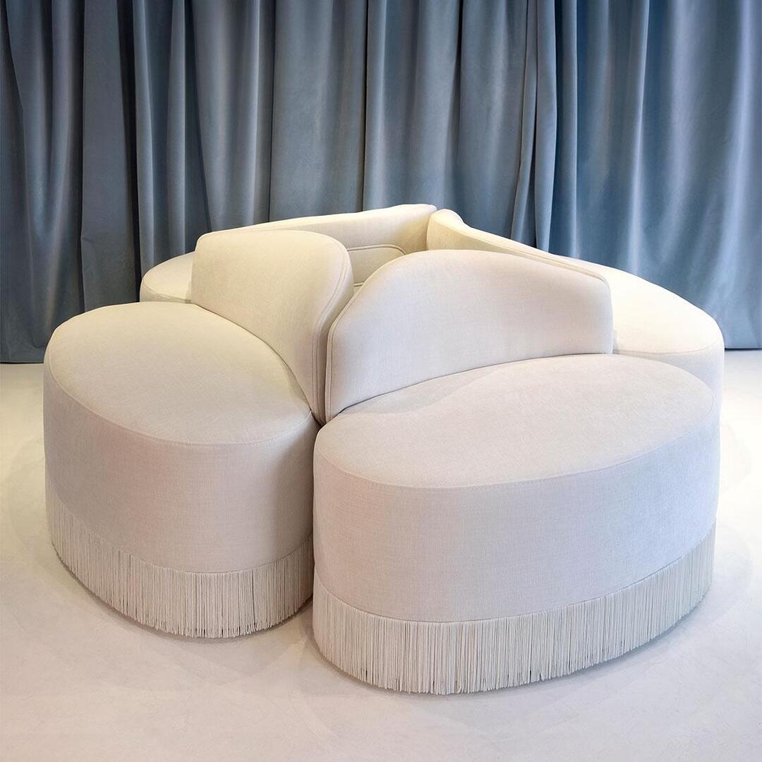Top view of a set of four white Doris Armchairs upholstered in chenille, with tricotine fringes and a blue curtain in the background.