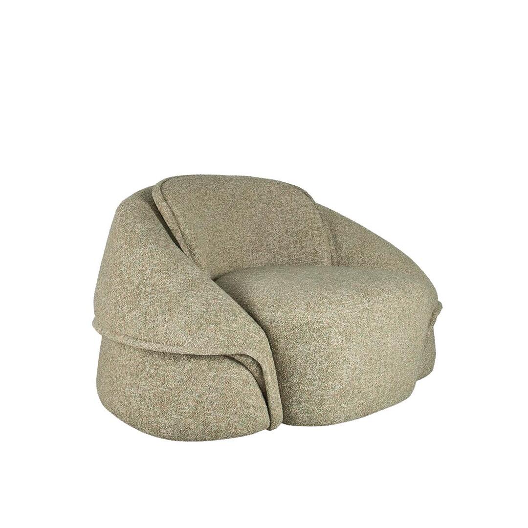 Three-quarter front view of the Romy armchair, emphasizing its depth and the voluminous, wrap-around design of the armrests. The Lierna fabric's coarse, tactile weave is visible, following the fluid curves of the chair's Art Deco-inspired profile.