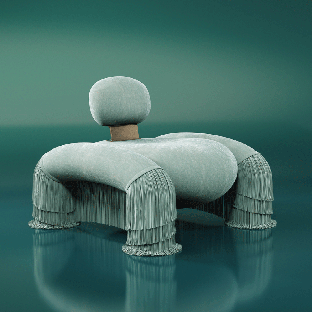 45-degree front view of the Odessa Armchair with a moving backrest and fringes. Upholstered in Dedar Plushy 147 and Sirgaria Castro Seda 111, paired with aged brass. Set against a green-blue background.