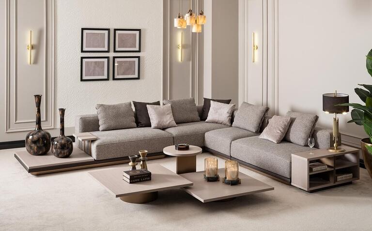 Contemporary living room with sleek sectional sofas in light tones, set against a panoramic city skyline through floor-to-ceiling windows.
