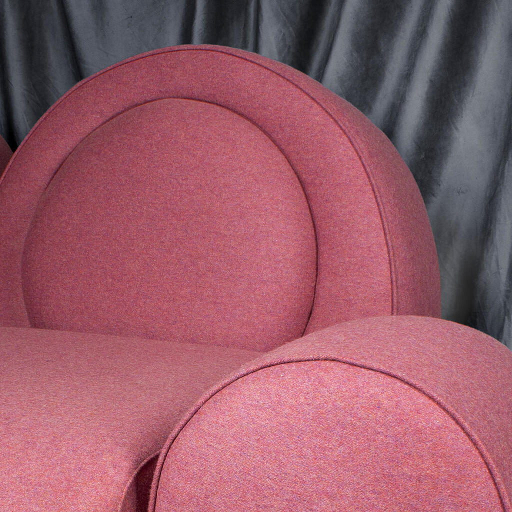Simone armchair detail, upholstered in pink fabric, against a blue velvet curtain.