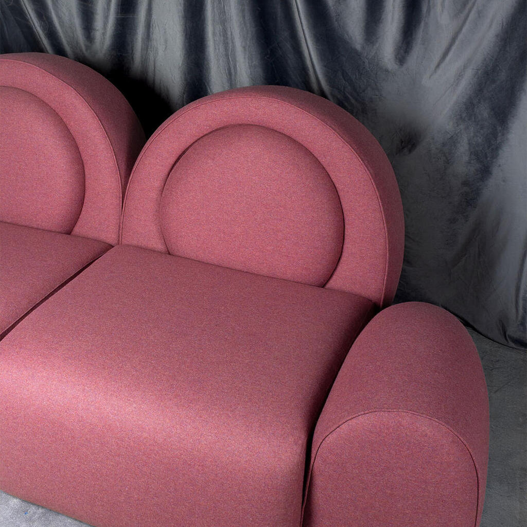 Simone sofa detail, upholstered in pink fabric, against a blue velvet curtain.