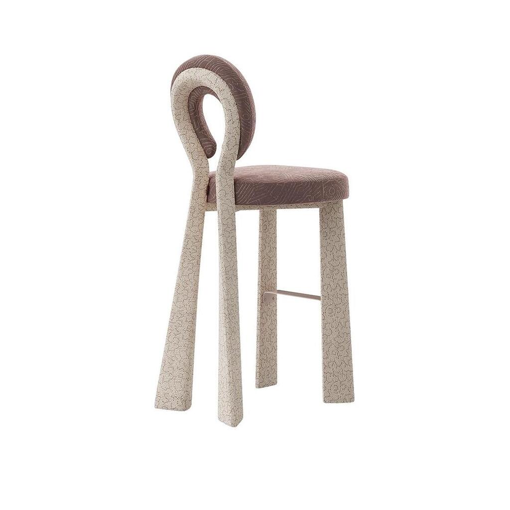 Three-quarter rear view of the Mary Bar Chair featuring a sculptural open-back design. The frame is upholstered in a textured cream bouclé, while the circular backrest and seat are dressed in a dusty-rose velvet with a subtle geometric pattern.