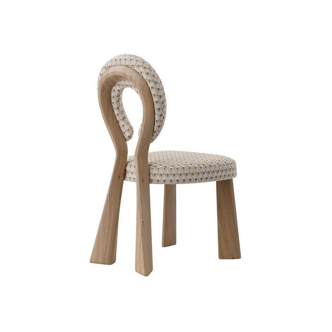 Three-quarter rear view of the Mary Dining Chair featuring a natural wood frame, emphasizing the organic curves of the sculptural open-back paired with patterned upholstery.