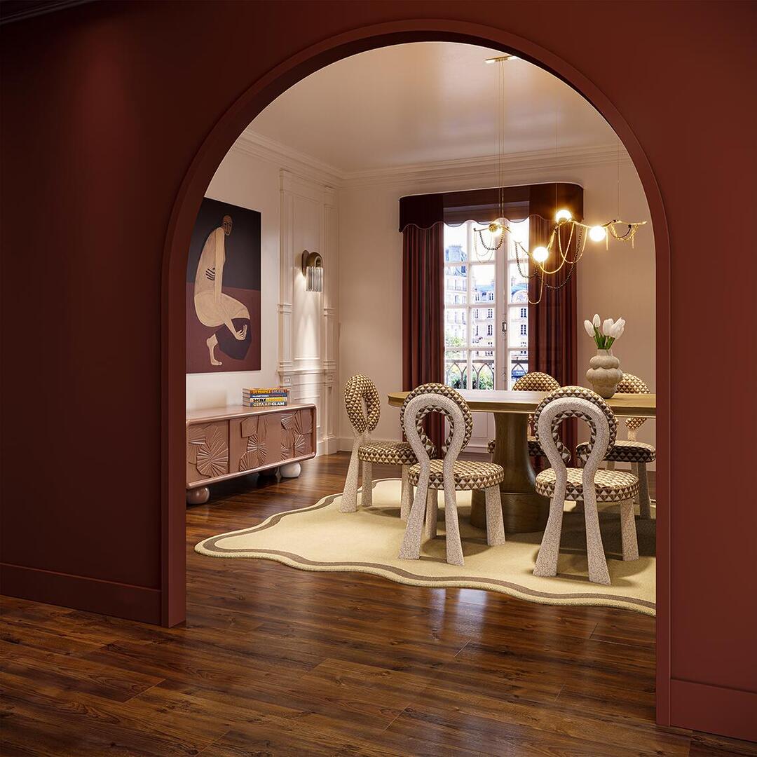 A view through a deep terracotta-red archway into a sophisticated, eclectic dining room. The space features a set of Mary dining chairs with unique looped backrests and patterned upholstery surrounding a Buck Oval dining table. Above the table hangs the sculptural, branching Berlin suspension lamp, while a Silo wall lamp provides soft accent lighting next to a modern figurative painting. To the left, a textured Mon Ooh sideboard in a dusty rose finish sits against a white paneled wall, all tied together by a wavy-edged cream rug on dark wood floors.