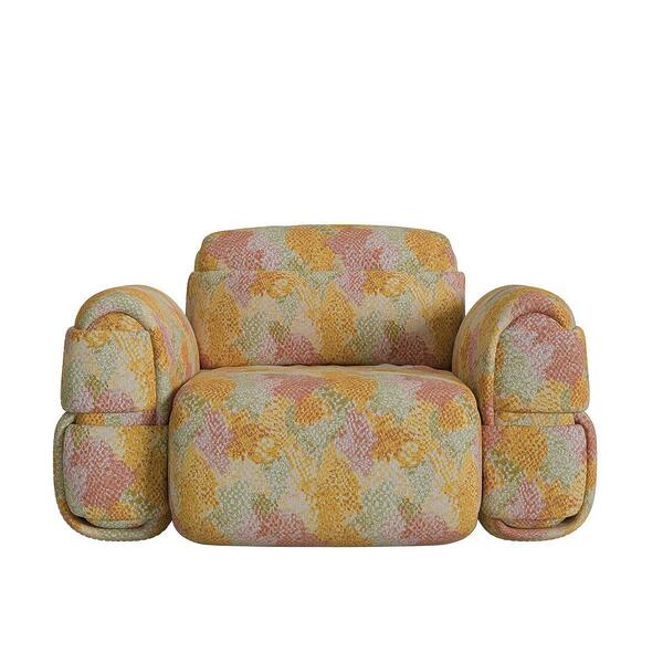 The Elsa Armchair, a bold and sculptural lounge chair featuring a voluminous, rounded design. Entirely upholstered in a vibrant, multi-colored patterned fabric with shades of yellow, orange, and green, the chair boasts oversized, cushioned armrests and a thick seat, giving it a cozy yet avant-garde aesthetic.