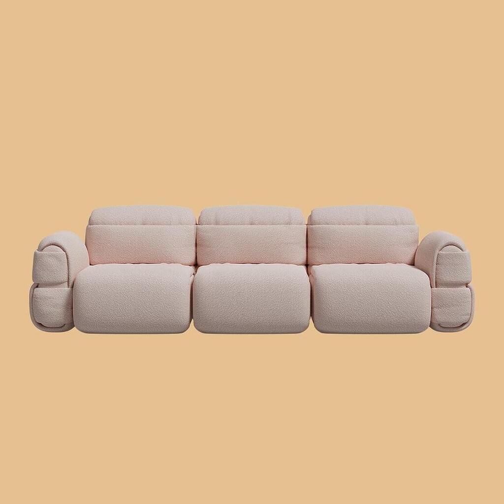 The Elsa Modular Sofa, viewed from the front. This three-seater sofa features a voluminous, rounded design composed of three central modules flanked by thick, segmented armrests. It is fully upholstered in a soft, light blush-pink textured bouclé fabric.