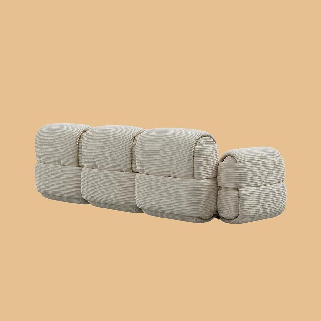 The Elsa Modular Sofa, viewed from a rear-angled perspective. This angle showcases the continuous sculptural profile of the three segmented backrests and the side of the thick armrest, entirely upholstered in an off-white, horizontally ribbed fabric.