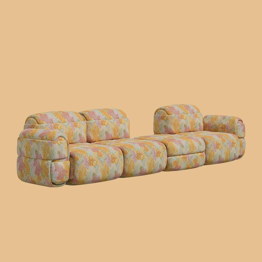 A wide modular configuration of the Elsa Sofa, showing two backrest modules with a large armless module and a separate seating section. The repetitive padded forms and the colorful patterned upholstery emphasize the deconstructed design.