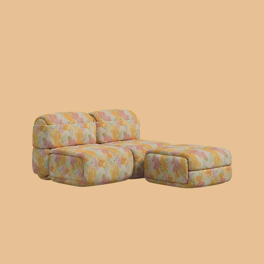 A compact L-shaped arrangement of the Elsa Modular Sofa, combining two backrest modules with a single armrest and an ottoman used as a footrest. Every surface is covered in the same textured abstract patterned fabric.