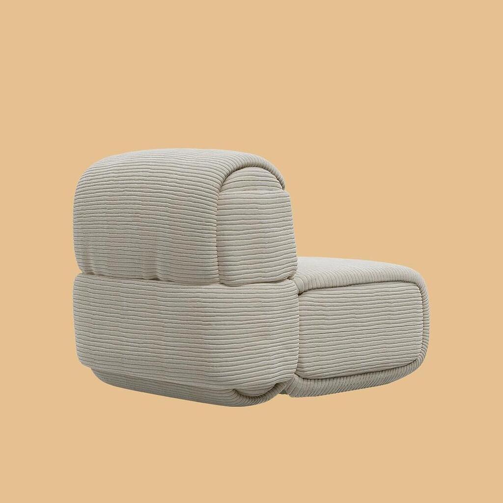 The Elsa Modular Armless Chair, shown from a side and back angle. The sculptural, pillowy profile of the segmented seat and backrest is clearly visible, fully upholstered in a textured, off-white horizontally ribbed fabric.