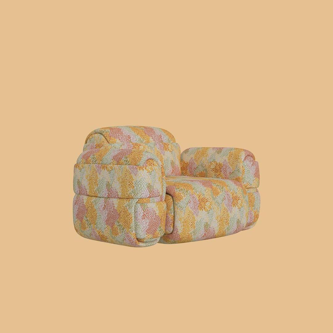 The Elsa Modular Armchair, viewed from a slight angle. This bold, bulky lounge chair features a central rounded seat and backrest, flanked by two oversized, segmented armrests. The entire piece is covered in a vibrant, multi-colored geometric patterned fabric in yellow, coral, peach, and sage green hues.