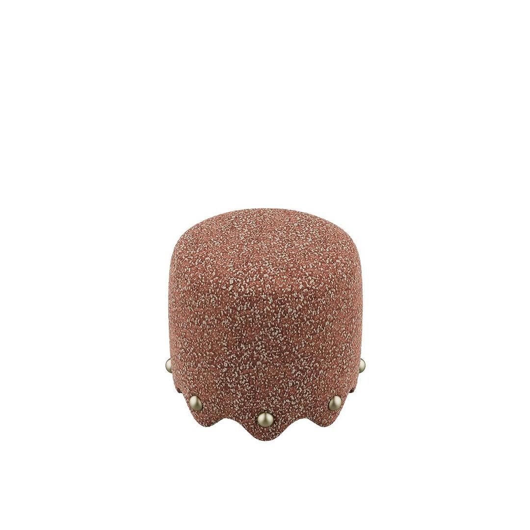 A high-angle perspective of the Bette Stool by Ottiu, highlighting the rounded volume and the dense, pebbled texture of the rust-colored Élitis Mochi upholstery. The decorative brass spheres are visible along the curved, wave-like base, adding a sophisticated, detail.
