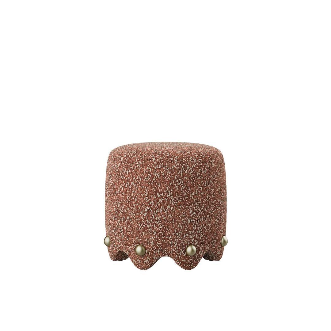 A low-angle shot of the Bette Stool by Ottiu, emphasizing its physical presence and the intricate scalloped detailing at the floor level. The rust-toned Élitis Mochi fabric provides a warm, matte finish that complements the reflective quality of the signature brass studs.
