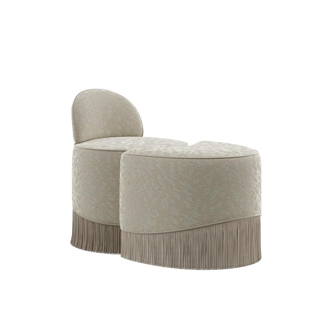A front-facing three-quarter view of the Lila Stool by Ottiu in an alternative fabric version. The modular sections feature a cream and beige animal-print textured fabric instead of the gold pattern. The structured backrest and crescent ottoman sections are nested together, completed by a matching neutral fringe skirt at the base.
