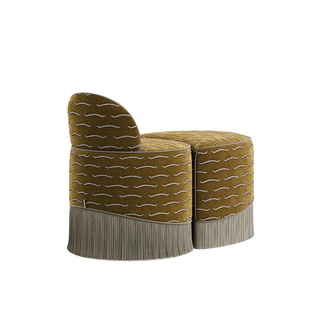 A three-quarter rear view of the Lila Stool by Ottiu in gold jacquard velvet. This angle shows the smooth, curved back of the low backrest section nested tightly against the matching crescent-shaped ottoman section. The neutral cream fringe flows seamlessly around the base of both pieces, and thin piping outlines the top edges.
