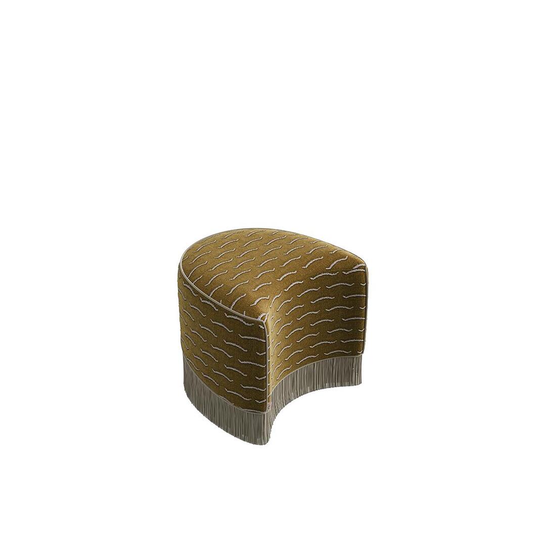 A high-angle view of the secondary modular piece of the Lila Stool by Ottiu, shown independently. This standalone ottoman section features a distinct crescent, curved-in silhouette upholstered in gold jacquard velvet, finished with a matching cream fringe base.
