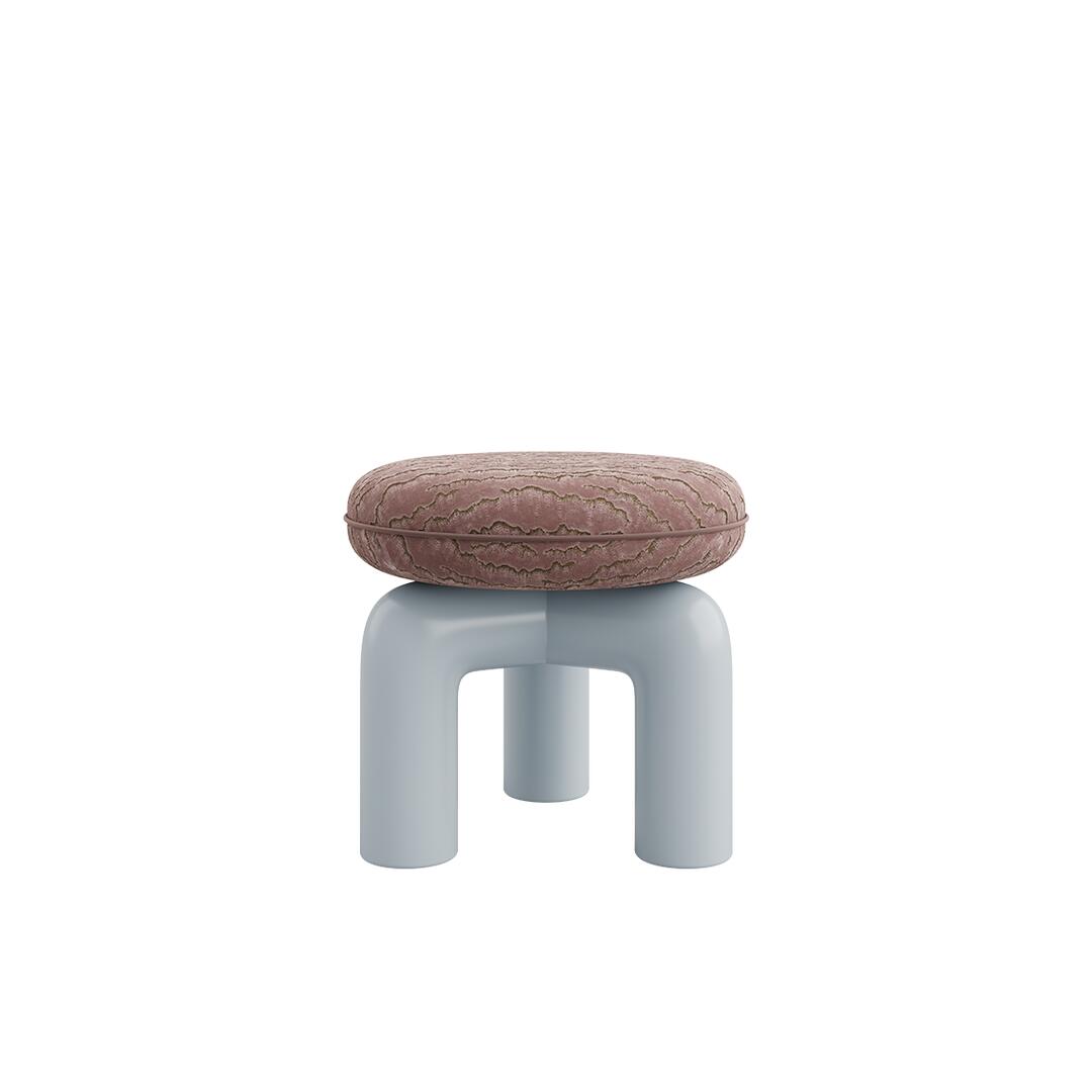 Straight-on eye-level view of an alternative colorway for the Tamara Stool by Ottiu. The round seat is upholstered in a dusty rose or mauve-toned embroidered velvet with subtle textured patterns. It is paired with a sculptural, glossy base featuring three thick, tubular arches in a light blue-grey lacquered wood finish.