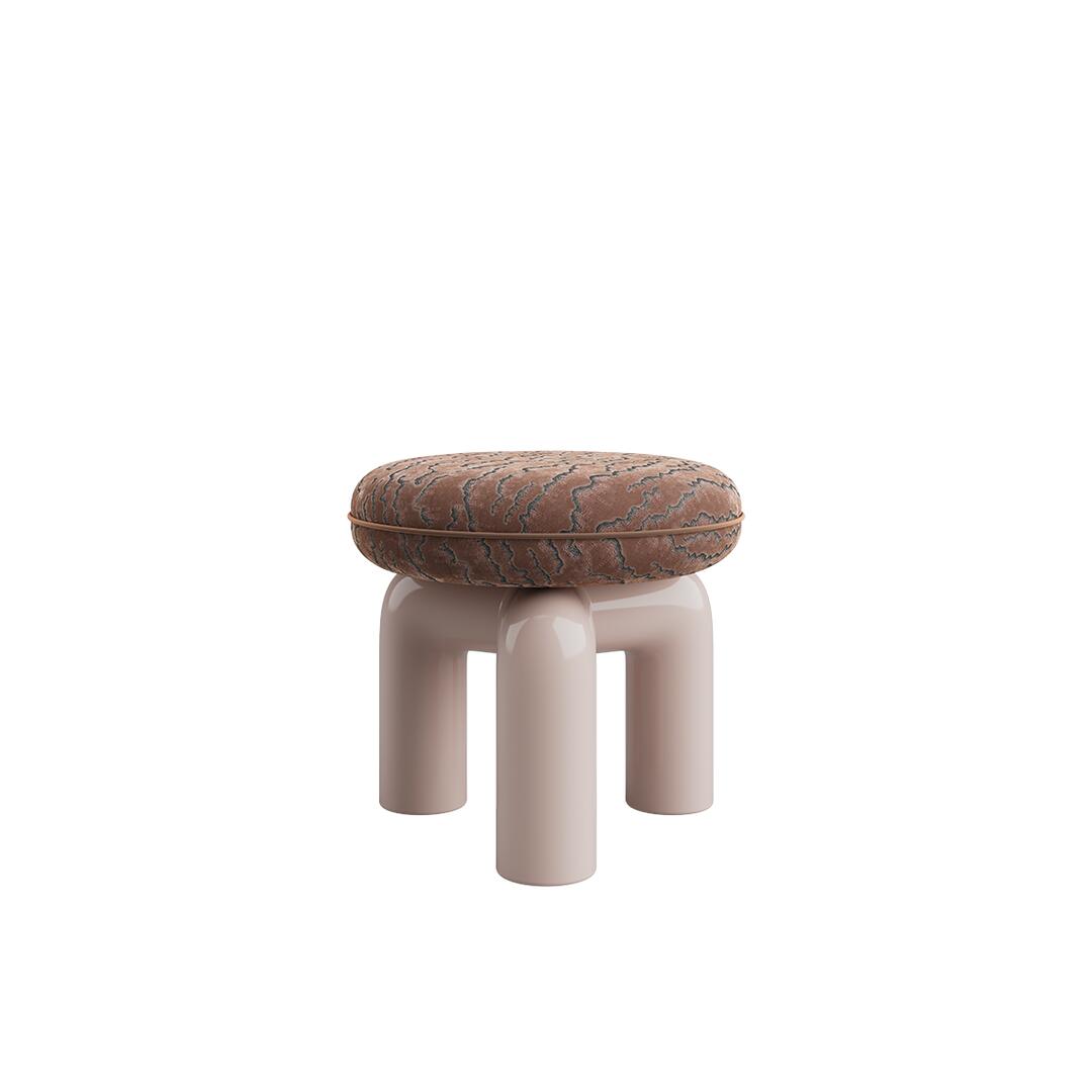 A three-quarter perspective view of the Tamara Stool by Ottiu, showcasing its architectural depth. The round, cushiony seat is wrapped in a dark brown embroidered velvet with prominent organic textures and a finished piped edge. The glossy, light pink lacquered wood base clearly reveals how the three thick, tubular legs arch upward and join together in the center.