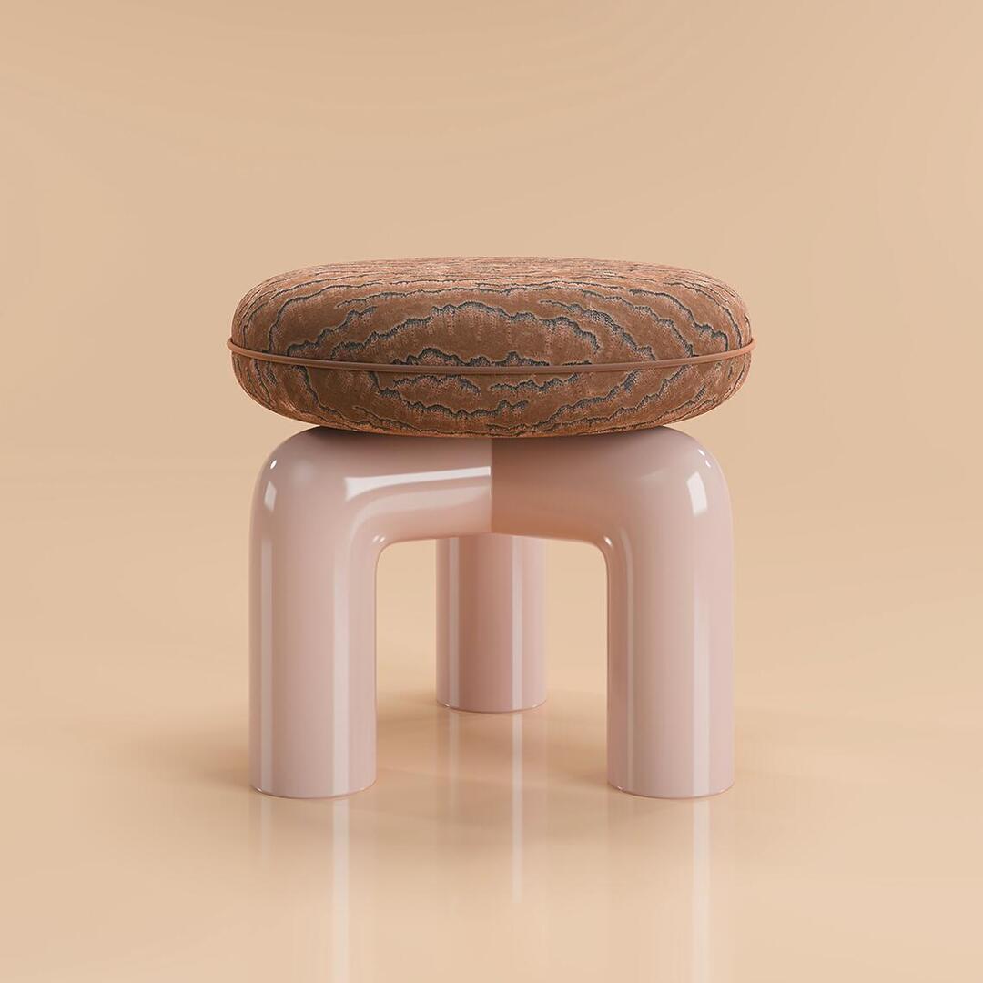 A full studio shot of the Tamara Stool by Ottiu, centered against a seamless, warm beige background. The stool features an architectural design with three thick, tubular legs made of glossy, pale pink lacquered wood that arch inward to form the base. Atop the base sits a thick, circular, plump cushion upholstered in a textured embroidered velvet with a brown and dark grey wavy pattern. A crisp velvet piping runs horizontally around the middle of the seat. The polished finish of the base creates clean, subtle reflections on the glossy floor beneath it.