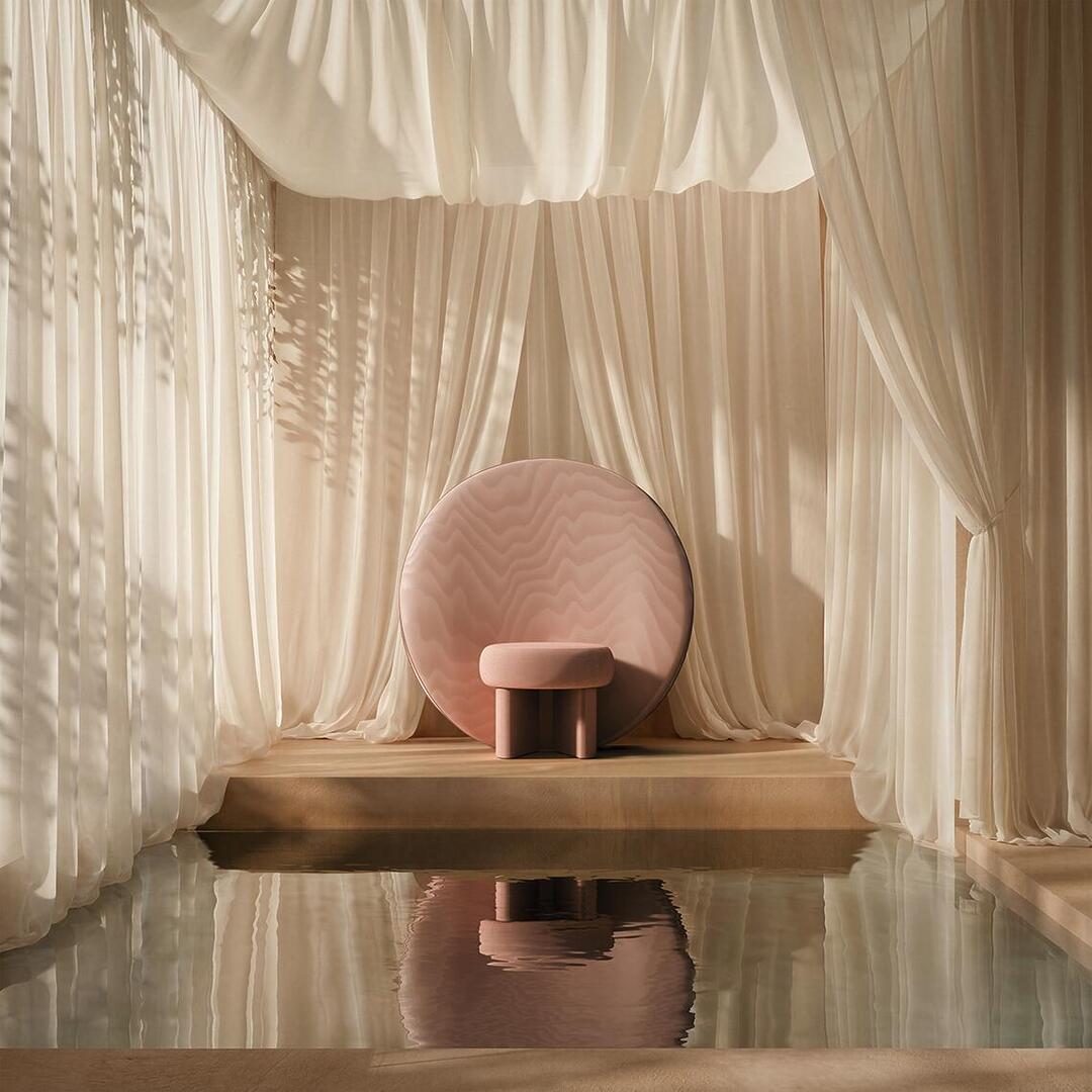 The dusty rose Solène Armchair elevated on a wooden platform inside a serene, dreamlike indoor pool setting, surrounded by flowing, translucent white curtains that reflect softly in the water.