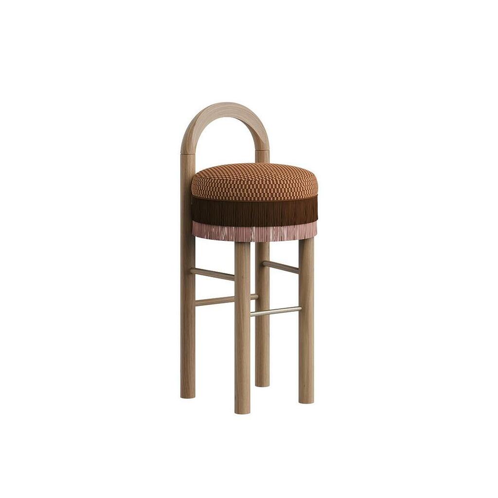 Three-quarter view of the Ann Bar Chair featuring natural wood legs, a decorative weave pattern seat cushion, layered brown and pink fringe details, an arched wooden frame backrest, and a stainless steel footrest.