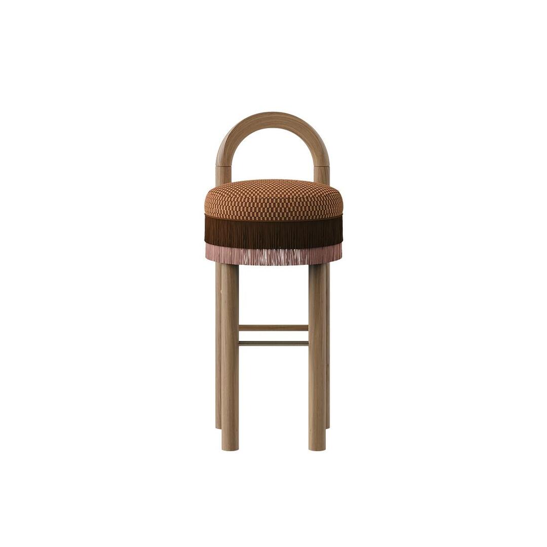 Front view of the Ann Bar Chair with natural wood legs, an arched backrest structure, a decorative weave patterned seat cushion, layered fringes in dark brown and soft pink, and a stainless steel footrest.
