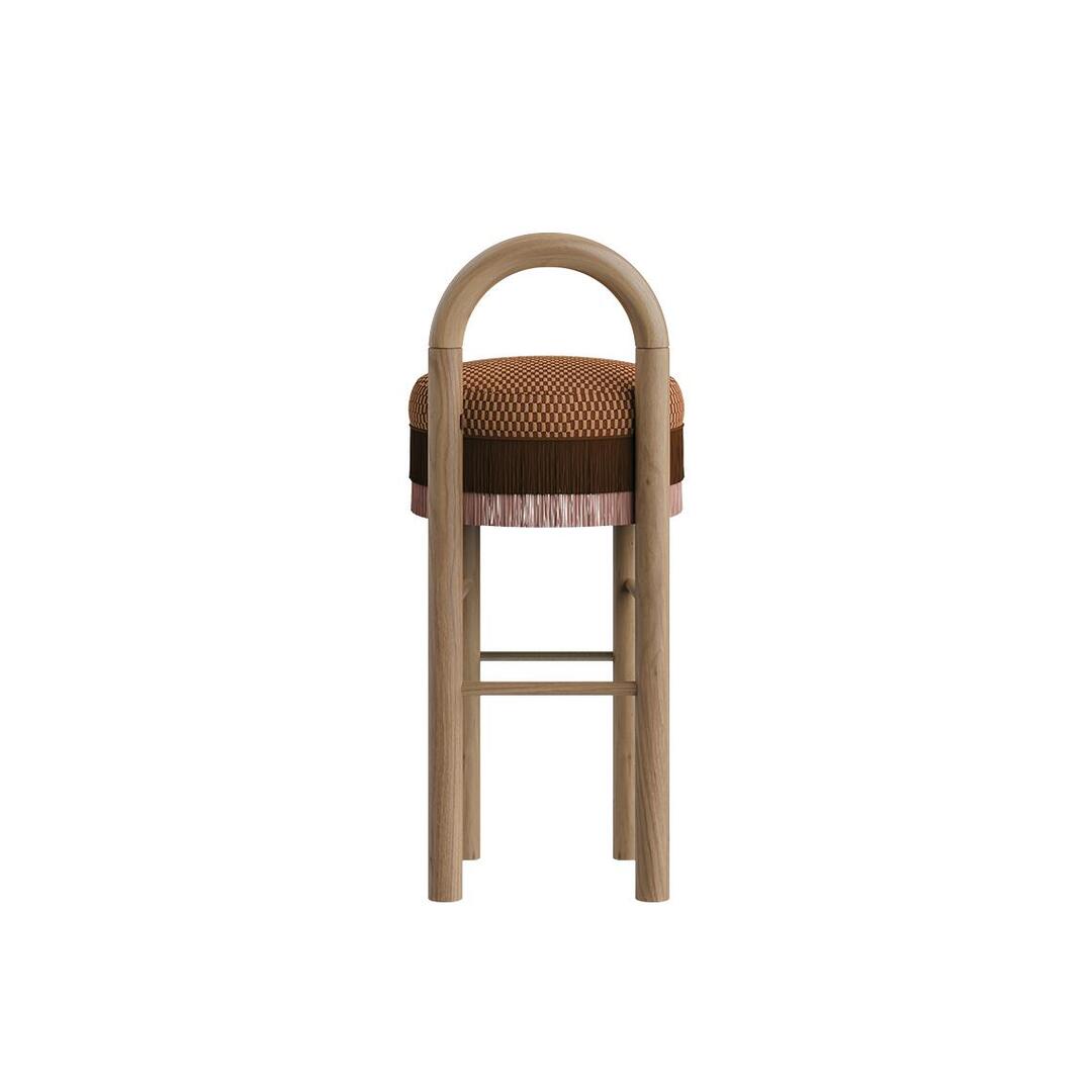 Back view of the Ann Bar Chair featuring the curved natural wood frame backrest, layered fringe details around the upholstered seat cushion, and stainless steel footrests.