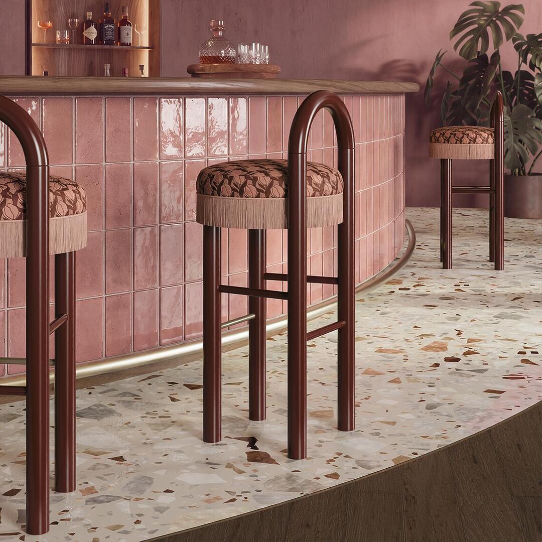 Ann Bar Chairs with dark lacquered wood frames and patterned upholstery arranged along a pink tiled bar counter over terrazzo flooring.