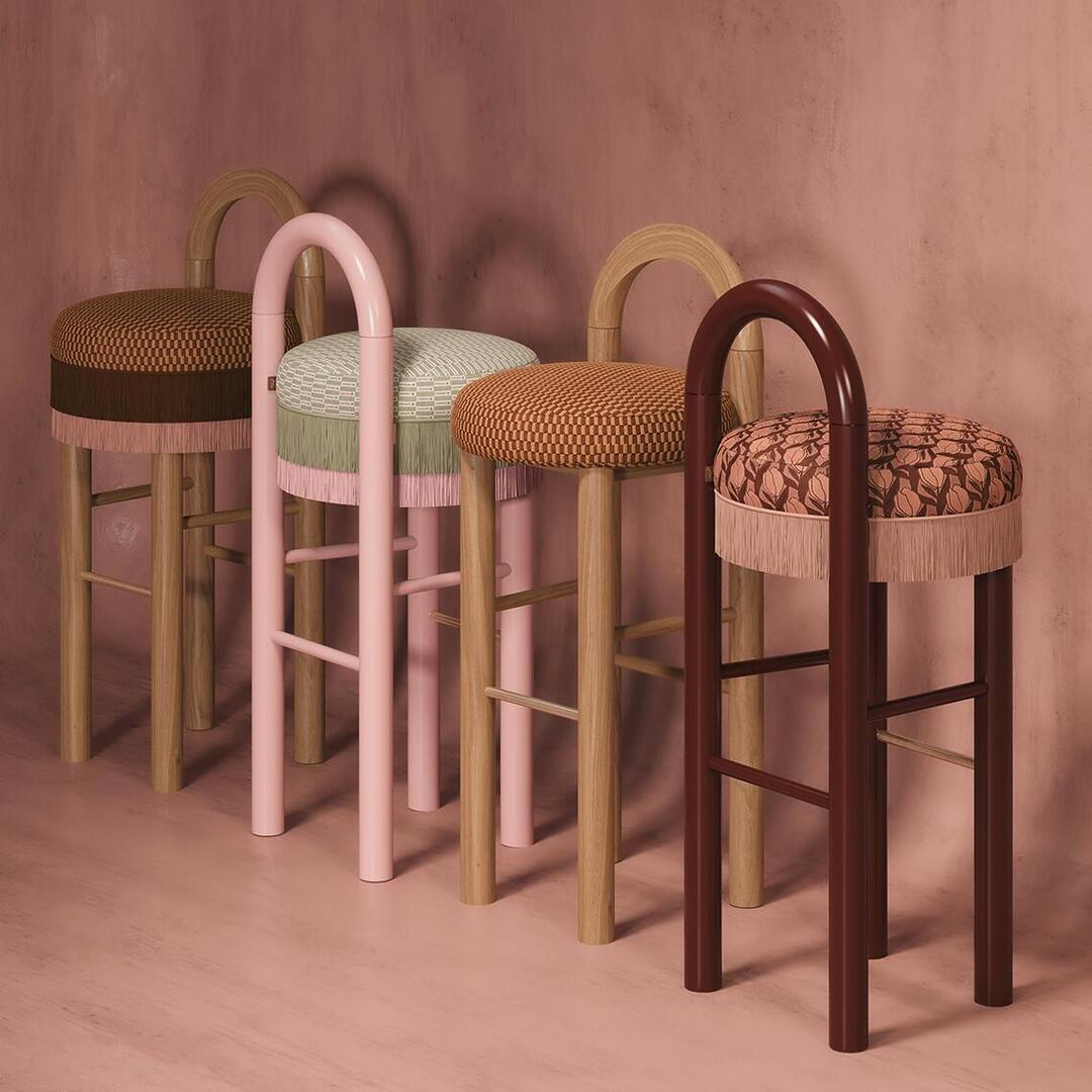 "Lineup of four Ann Bar Chairs showcasing various finish combinations, including natural wood, pink lacquer, and dark wood frames with fringed upholstery.