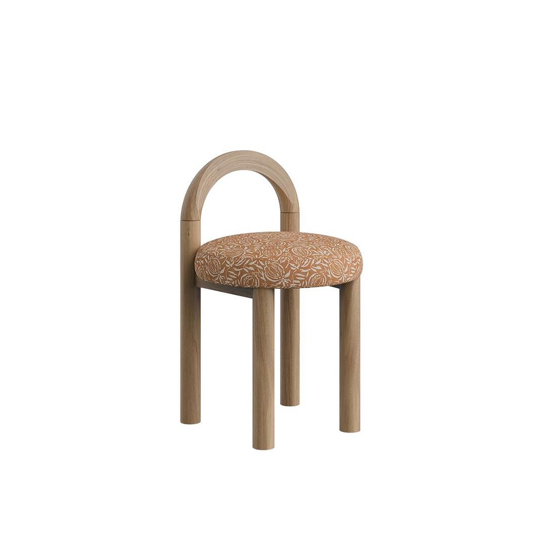 Angle view of the Ann dining chair without fringes, featuring cylindrical natural wood legs, an arched backrest, and an upholstered pattern seat.