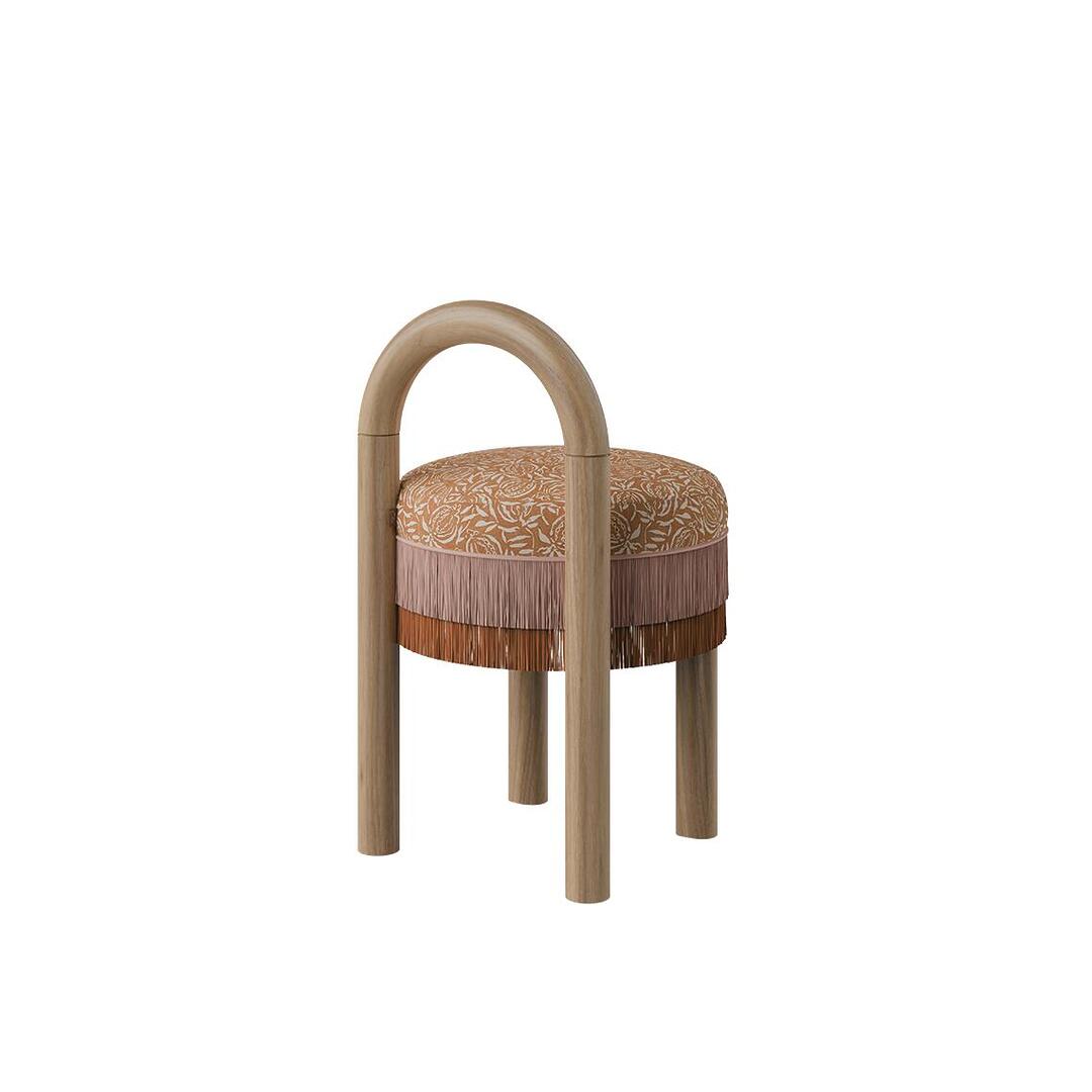 Three-quarter side view of the Ann dining chair showcasing its tubular natural wood frame, patterned fabric seat, and soft fringe detail along the apron.